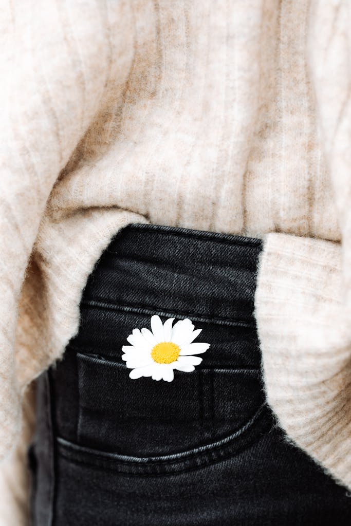 A white daisy flower peeking from the pocket of black jeans, paired with a cozy sweater.