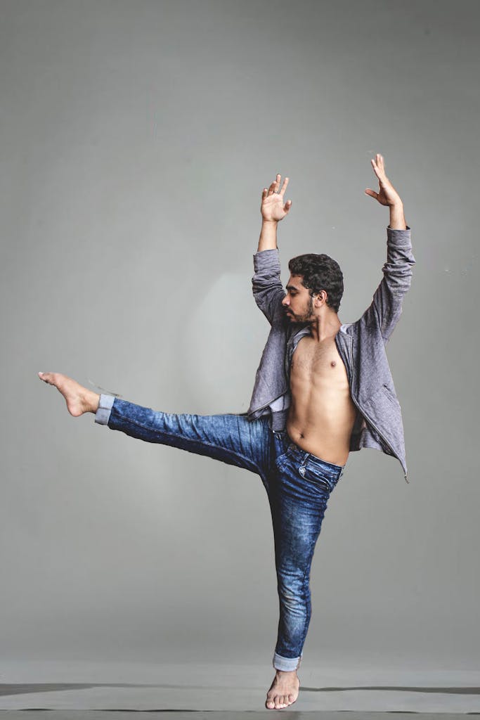 Male dancer in mid-movement, showcasing flexibility in denim jeans against a gray background.